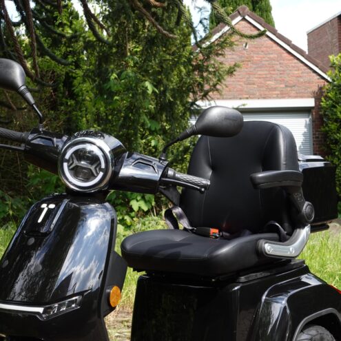 aanzicht van een zwarte scootmobiel buiten bij het gras met veiligheidsgordel puramobi